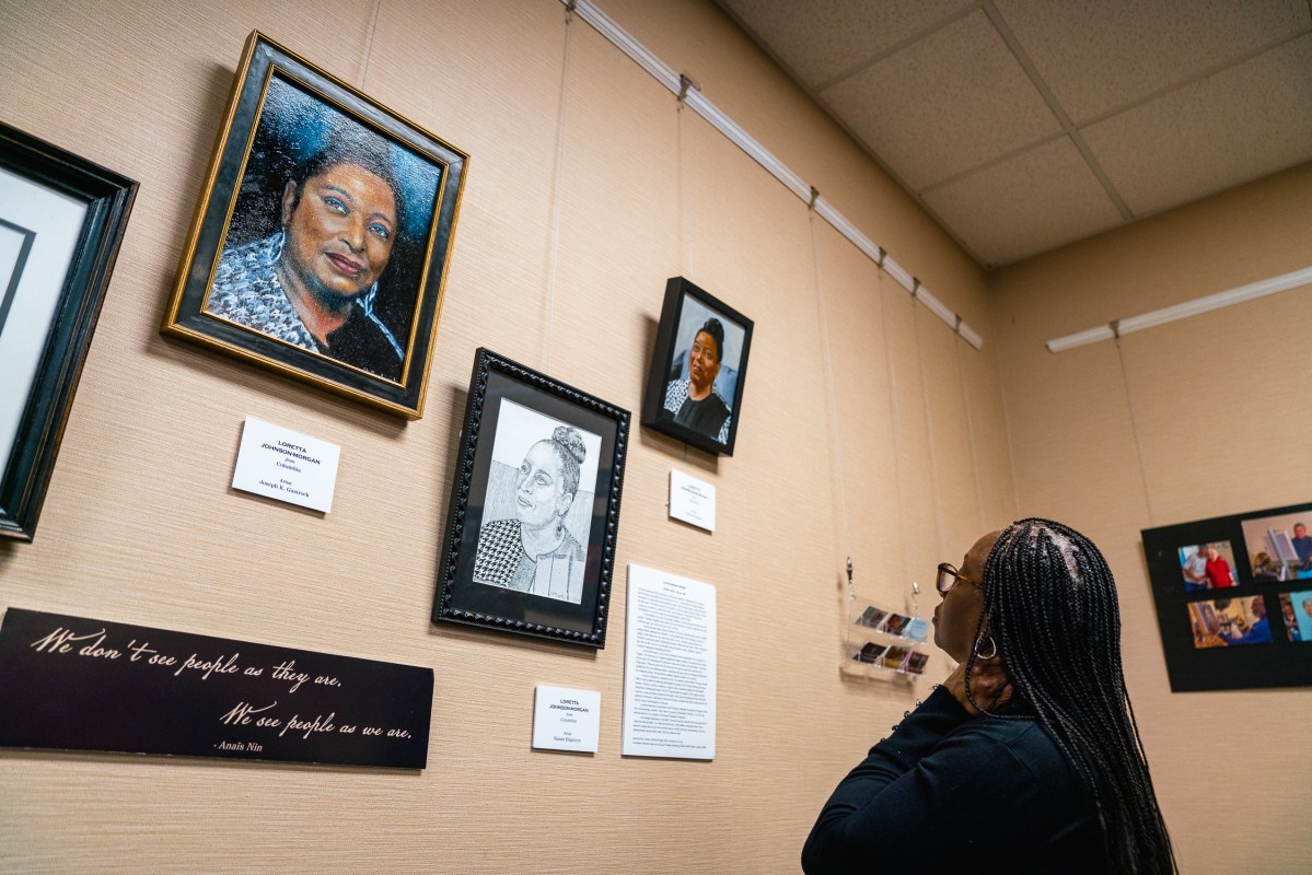 A woman looks up at a set of portraits and text hanging on a wall.
