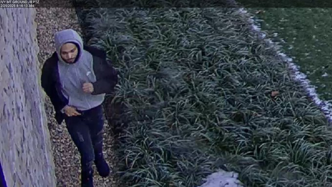 A man in a grey hoodie walks past a wall in a field