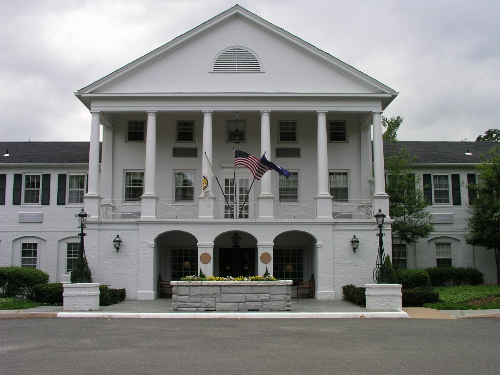 A facade of a large white building with three archways, columns, and flags hanging above the front doors.