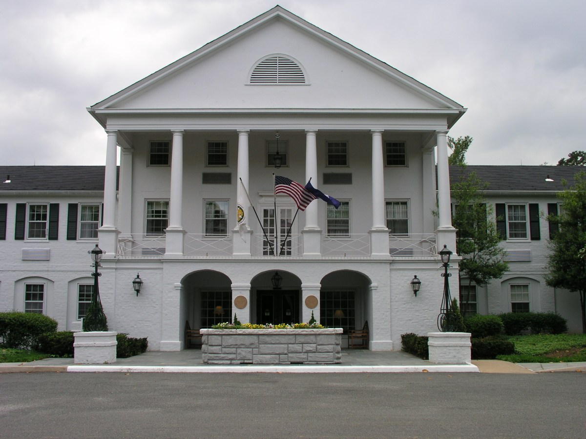 A facade of a large white building with three archways, columns, and flags hanging above the front doors.
