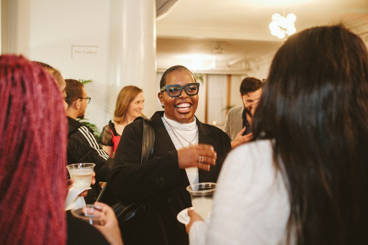 A person wearing glasses in a group, smiling, with people standing around holding cups of beverages.