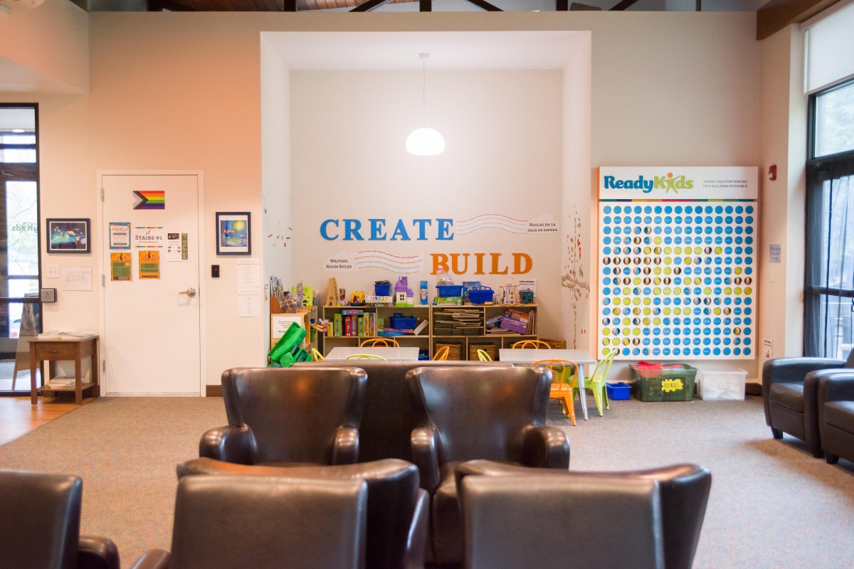 An empty waiting room filled with large leather chairs. Text on the wall reads "Create" and "Build." There are shelves filled with toys and art supplies.