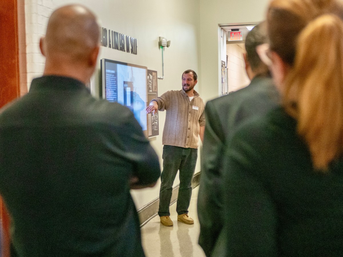 A person pointing at a screen with others looking on, blurry in the foreground of the image.