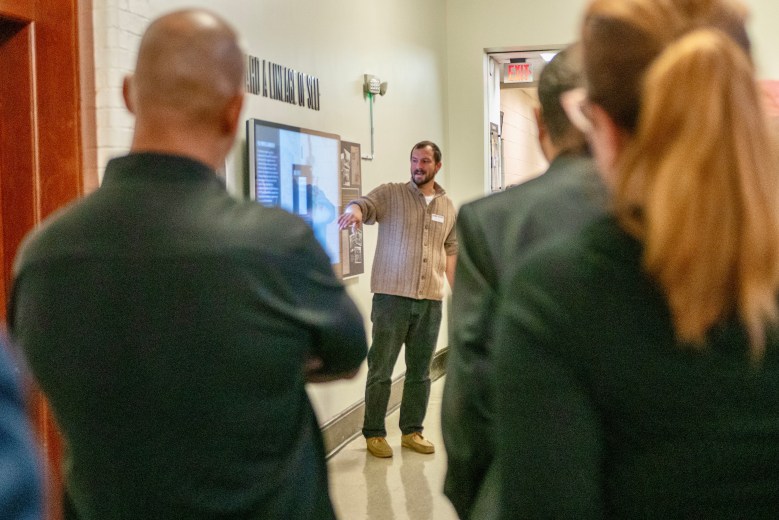 A person pointing at a screen with others looking on, blurry in the foreground of the image.