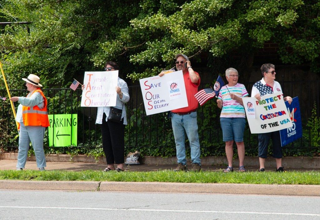 Five people stand on a sidewalk holding signs reading "save our social security" and "protect the constitution of the USA." Trees are visible behind them.