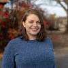 A woman in a blue sweater in front of fall leaves