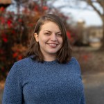 A woman in a blue sweater in front of fall leaves