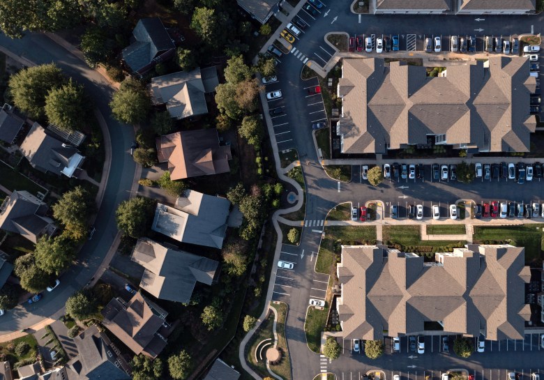 An aerial view of a neighborhood showing roofs, lush green lawns, and parking spaces.