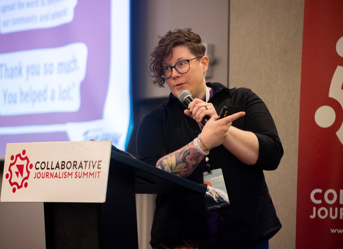A person holds a microphone at a podium that says "Collaborative Journalism Summit."