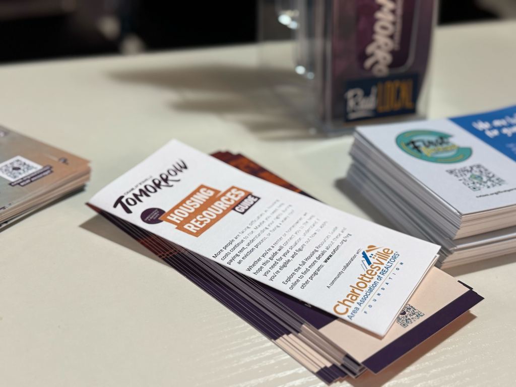 Brochures on a white table, including one that has a purple and orange logo that says "Housing Resource Guide."