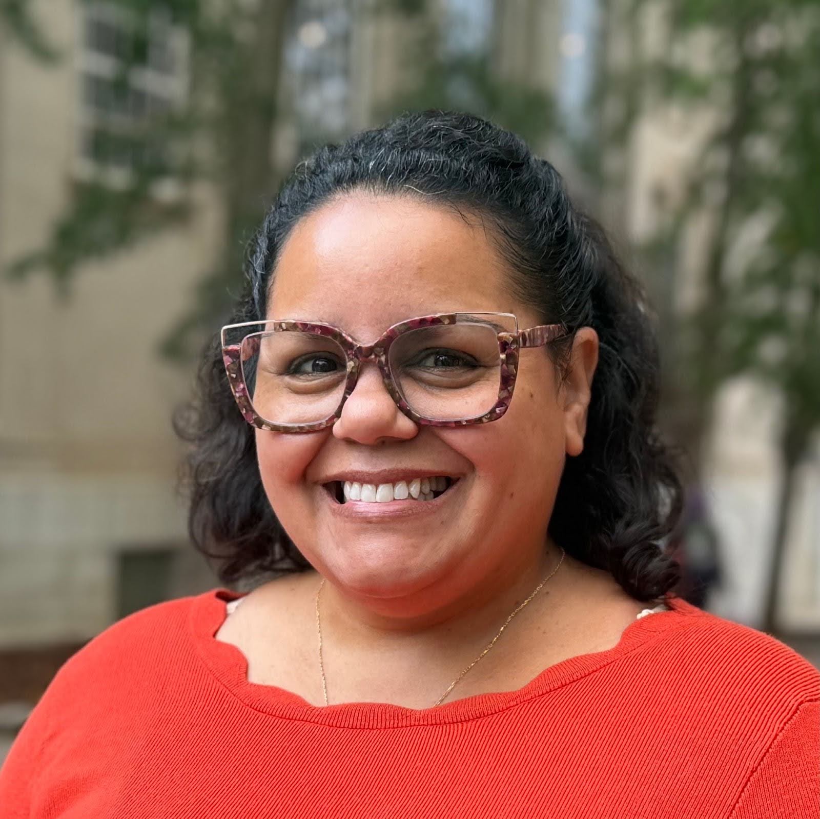 A woman in glasses and a red top smiles at the camera