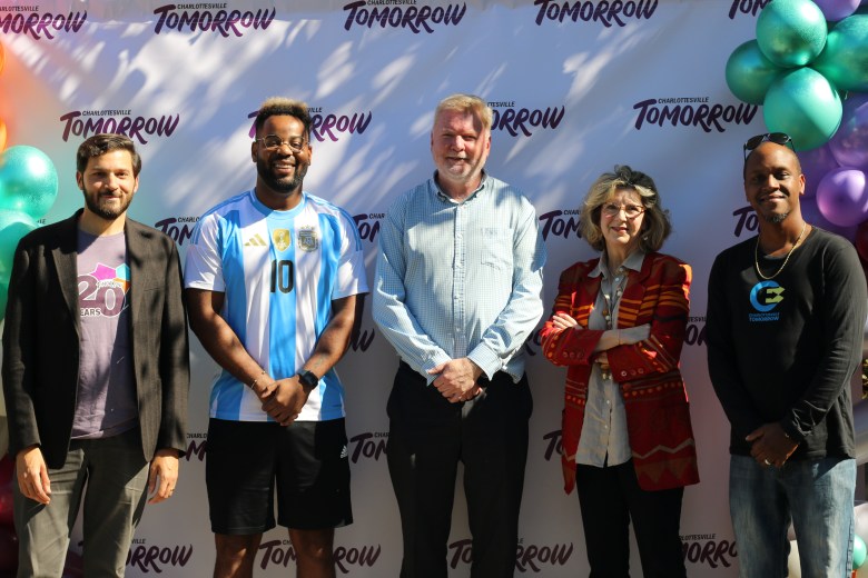 A group of five people. They smile and pose in front of a backdrop that says CHARLOTTESVILLE TOMORROW.