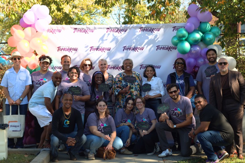 A group of people smile. They pose in front of a backdrop that says CHARLOTTESVILLE TOMORROW.