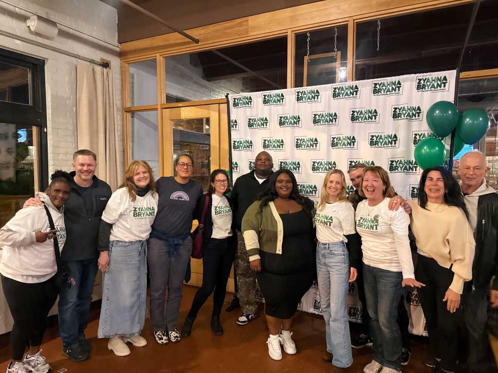 A group of people pose smiling for a photo behind a sign that reads, "Zyahna Bryant."