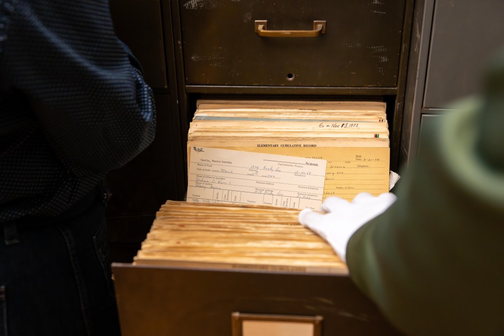 A photograph of an open file cabinet drawer, with a focus on an open file that says "Elementary Cumulative Record." The file contains a printed form, filled out by hand, for a student named Maxine Dorothy Harris. It shows that Harris was born on March 21, 1942 to William C. Harris and Mary Harris, and that the family's address was 1014 Grady Ave. in Charlottesville.