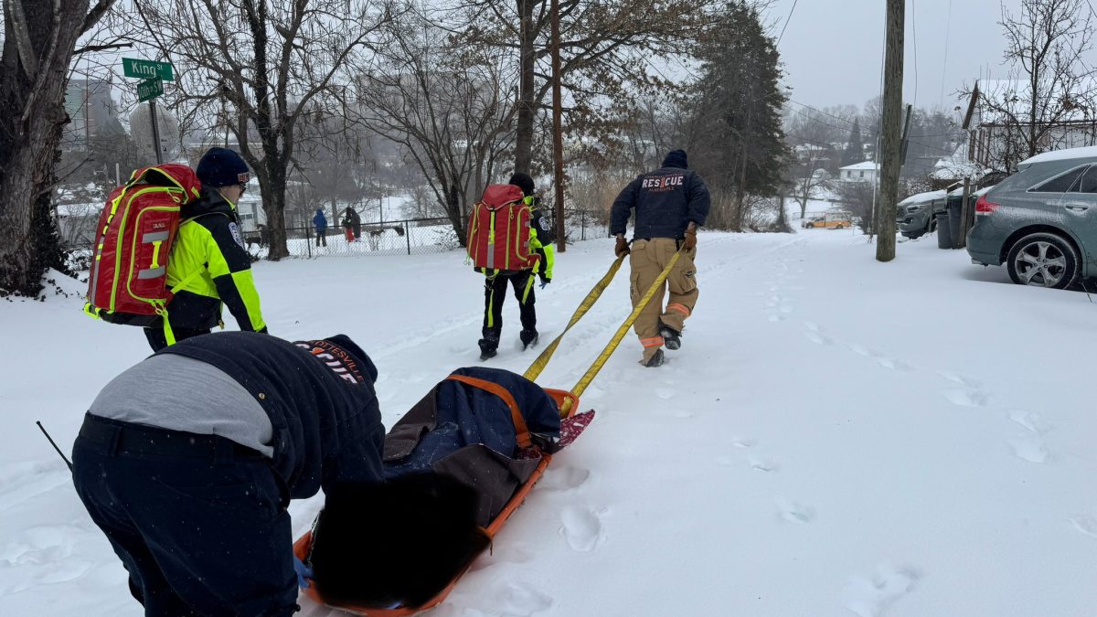 Rescuers are using a stokes basket, a stretcher designed for rescue in difficult terrain, as a sled on the snow, with one person pulling it by straps.