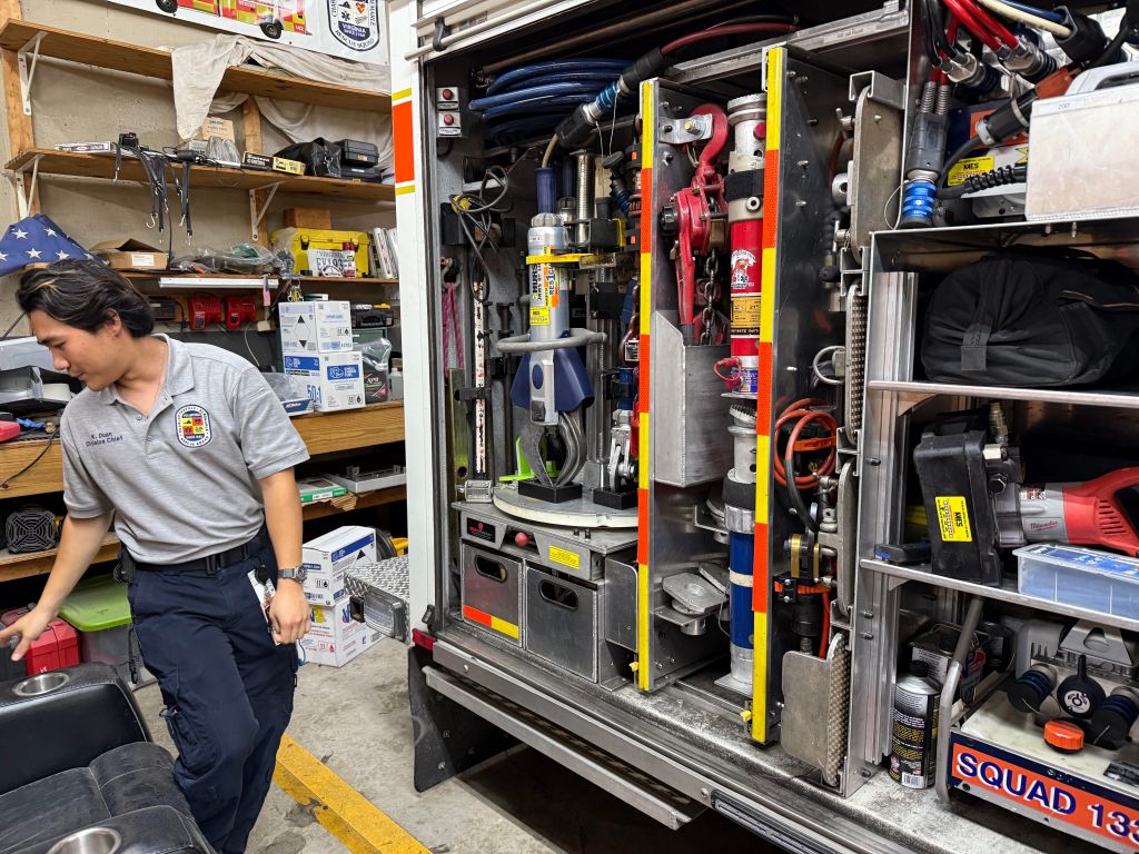 A man in a grey t-shirt with Charlottesville-Albemarle Rescue Squad logo on it is standing in a garage in front of a large open truck filled with various equipment.
