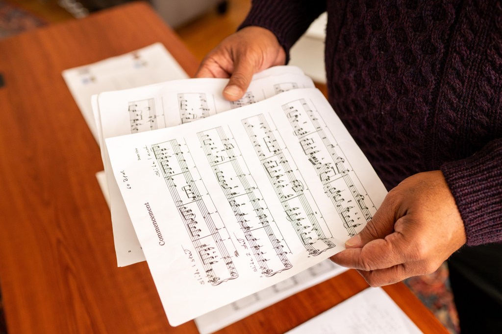 A photograph of a man's hands holding a few pieces of sheet music. The top sheet has the title "Commencement" printed at the top. "60bpm" is handwritten in the top right corner, and "slide 1 start" is handwritten just above the first measure of the music.