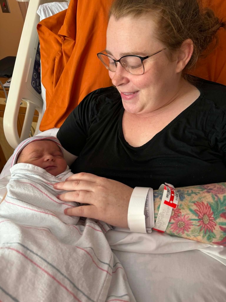 A woman holds a newborn baby in a hospital bed. She gazes at the baby lovingly.