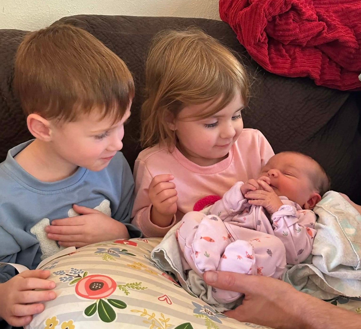 Two young kids looking lovingly at a newborn baby.