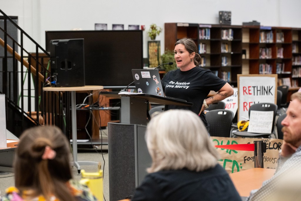 A woman stands at a podium and speaks to a group of who is listening.