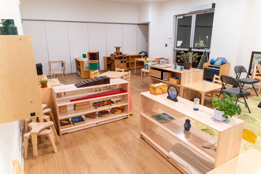 A room filled with wooden cubbies that have sensory learning tools, desks and stools.
