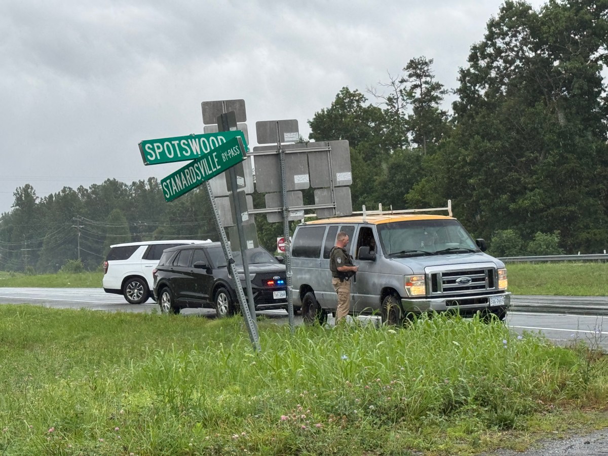 Two unmarked SUVs stop an older-model grey van at an intersection. A man dressed in khakis and a green top speaks to someone in the passenger seat.