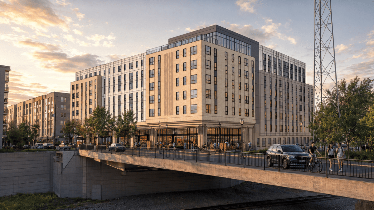 A realistic digital rendering of a proposed apartment building. The image shows how the eight-story building will sit within the immediate landscape, including other similarly-sized and similarly-designed buildings, a cell phone tower and a bridge.