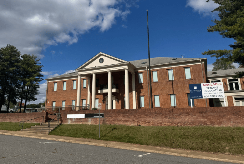 A large brick building with white columns is visible behind a low brick wall. A sign next to the building reads "Available, Tenant relocating."