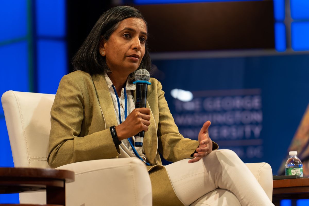 A woman seated in a white armchair speaks into a microphone.