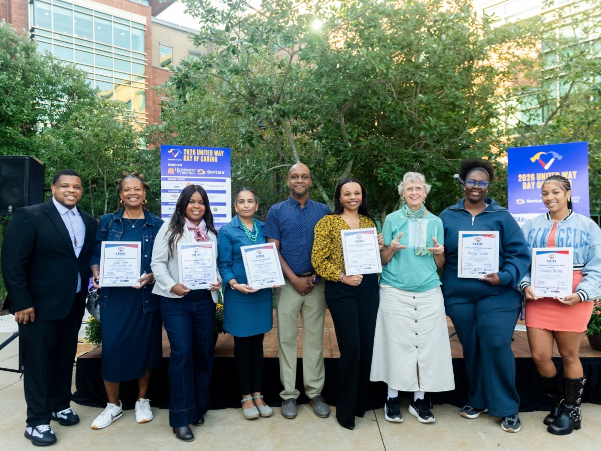 Nine people stand in a row in front of a stage. Most of them hold small, rectangular certificates.