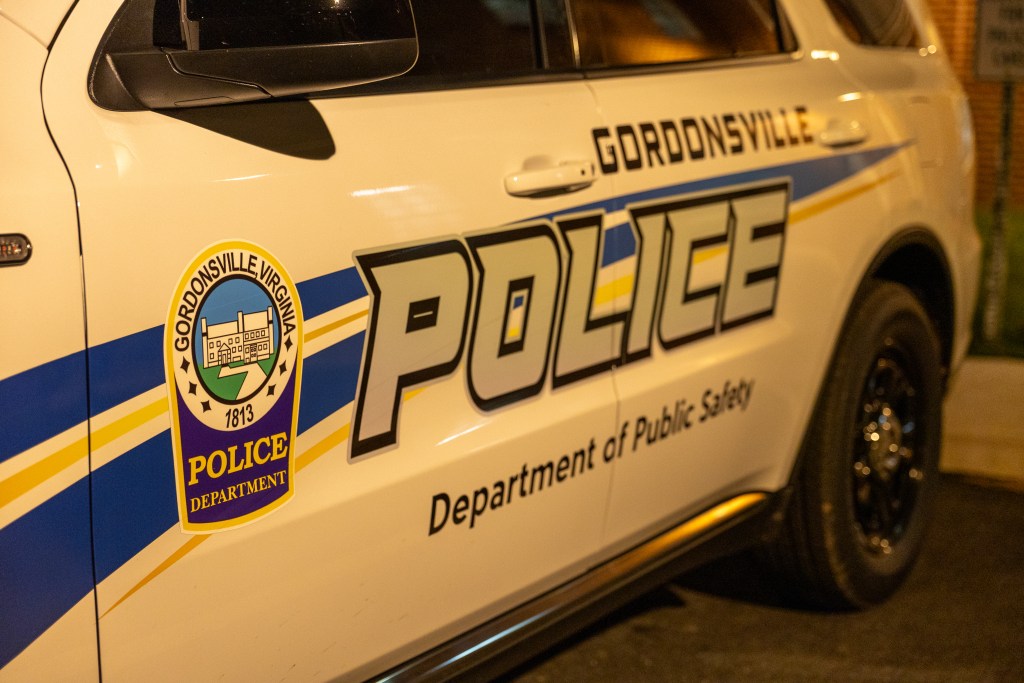 A closeup of a white police SUV at night under street lighting. The side of the SUV has a blue and gray decal that reads, "Gordonsville Police: Department of Public Safety."