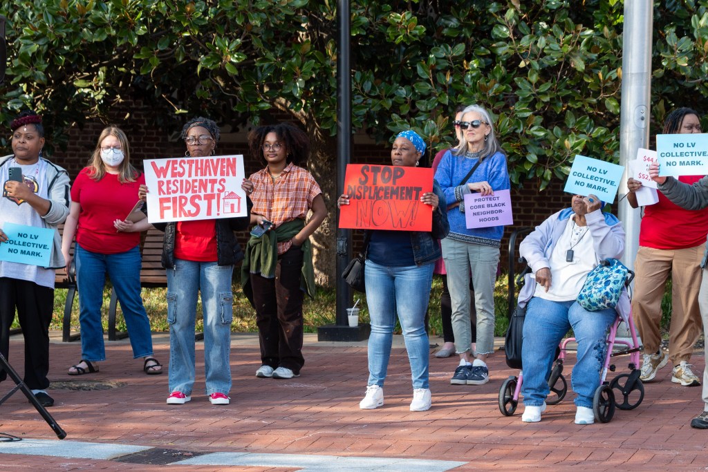 About 10 people stand outdoors at a rally, most holding signs. Two of the signs read "No LV Collective. No Mark." Another reads "Westhaven residents first!" Another says "Stop displacement now!"